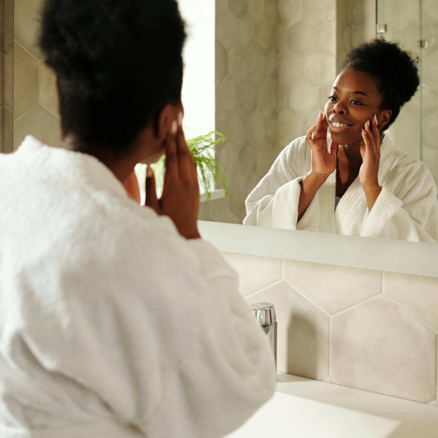 Black woman admiring her radiant even skin tone in mirror after skincare ritual